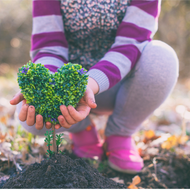 child bent down by a growing plant holding a heart that looks like a live plant